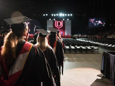 group of female students in graduation robes and mortarboards, walking into auditorium