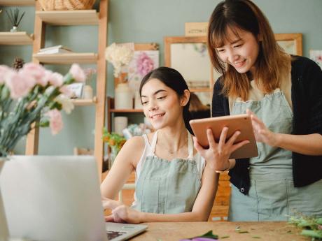 One flower shop employee completing online training on a computer while the other trains on a tablet.