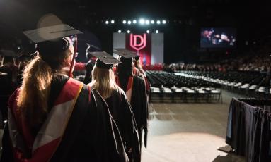 group of female students in graduation robes and mortarboards, walking into auditorium