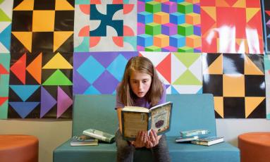 Student sits on bench reading a book in front of artwork