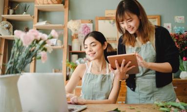 One flower shop employee completing online training on a computer while the other trains on a tablet.